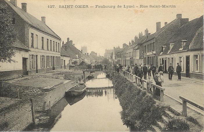 Cette rue du faubourg longe le watergang qui permet de se rendre dans les champs. On peut aperçevoir les petits ponts qui enjambe la rivière,et une bacove attachée sur le côté.