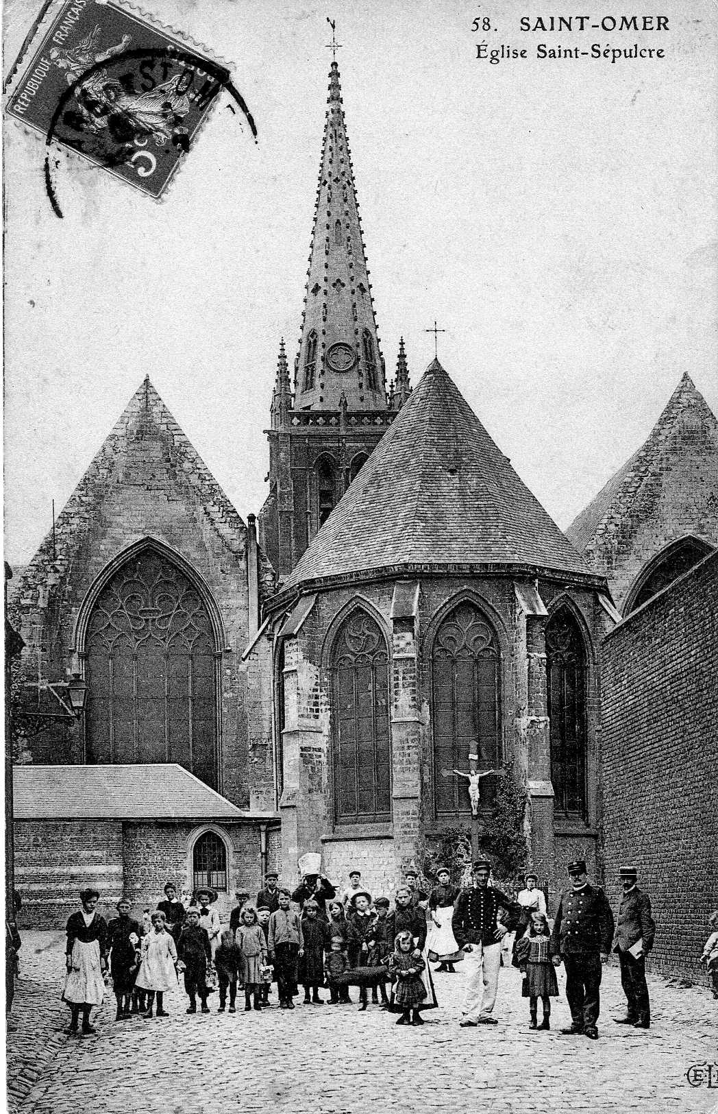 On voit bien les trois nefs qui sont d'une largeur à peu prés égale. Sur la droite de la carte se trouvait la prison de St Omer, on apeçoit le mur d'enceinte. Au premier plan il y a peut être un gardien de la prison en uniforme qui tient la main d'une petite fille ?